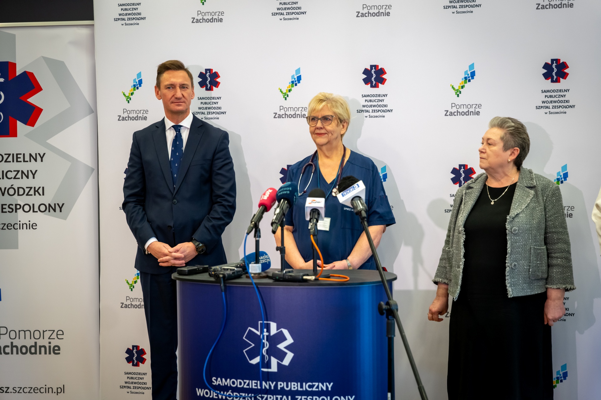 Konferencja prasowa w SPWSZ w Zdunowie - od lewej stoją na tle ścianki z logotypami szpitala i Pomorza Zachodniego - marszałek Olgierd Geblewicz, lek. Iwona Witkiewicz, kt&oacute;ra jest przy mikrofonie i dyrektor szpitala Małgorzata Usielska